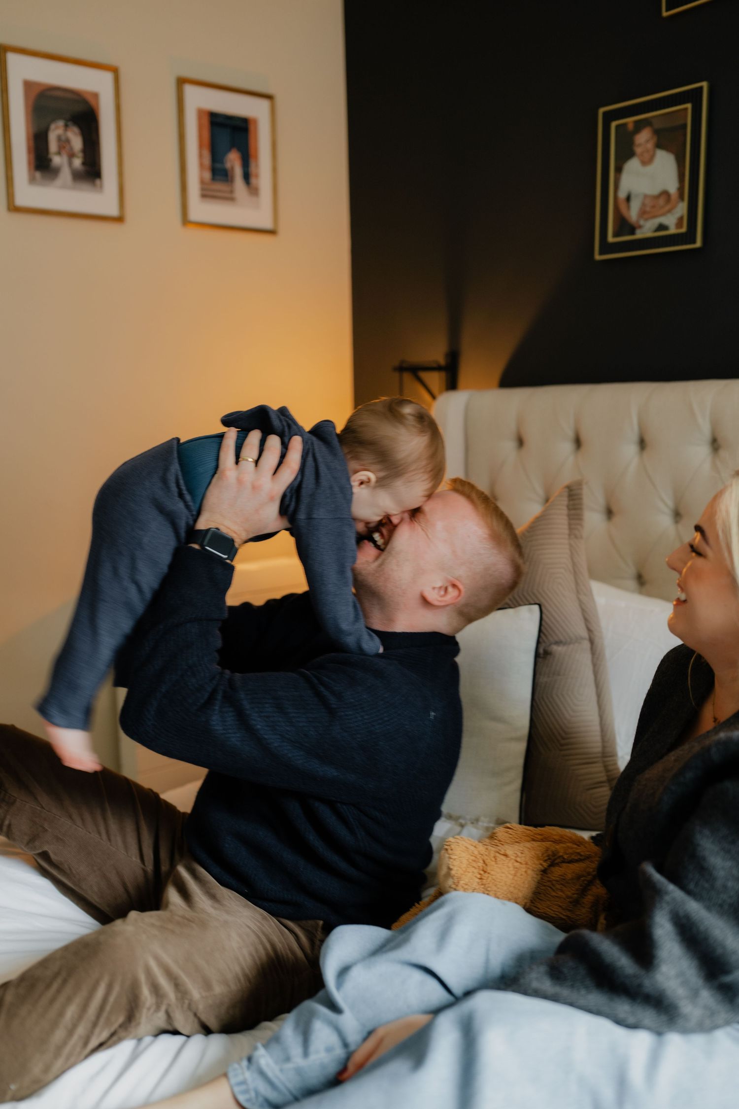 a fatherlifting his baby in the air while sited on the bed