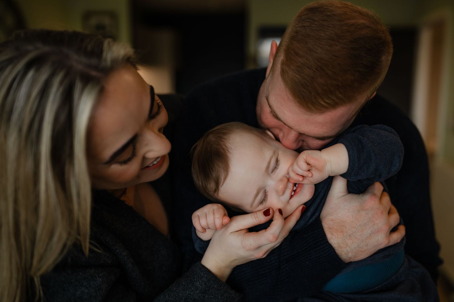 a close up of two parents holding their baby son close to their faces