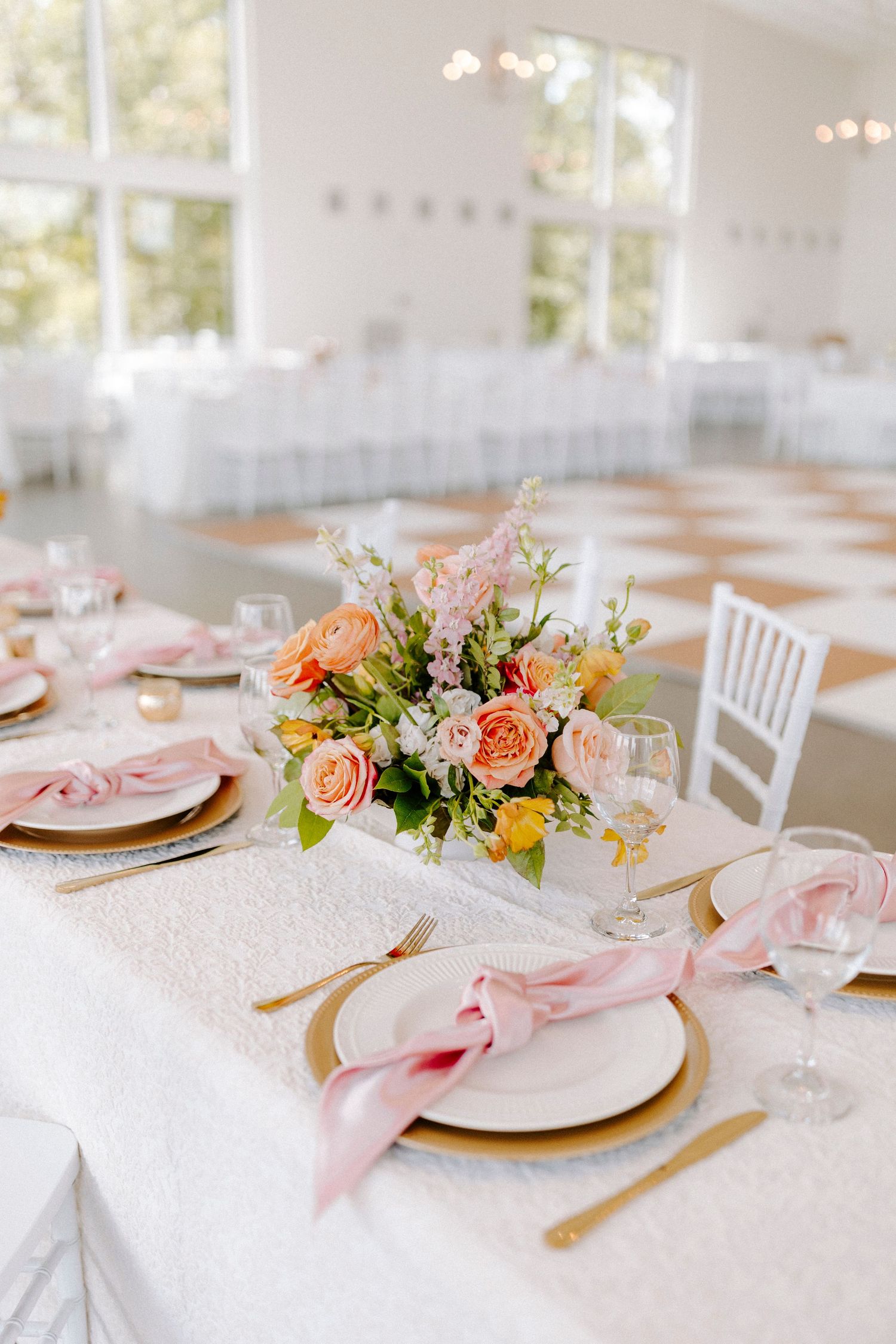 Elegant wedding reception table settings at Osage House with pink and peach floral centerpieces, white linens, and gold flatware.