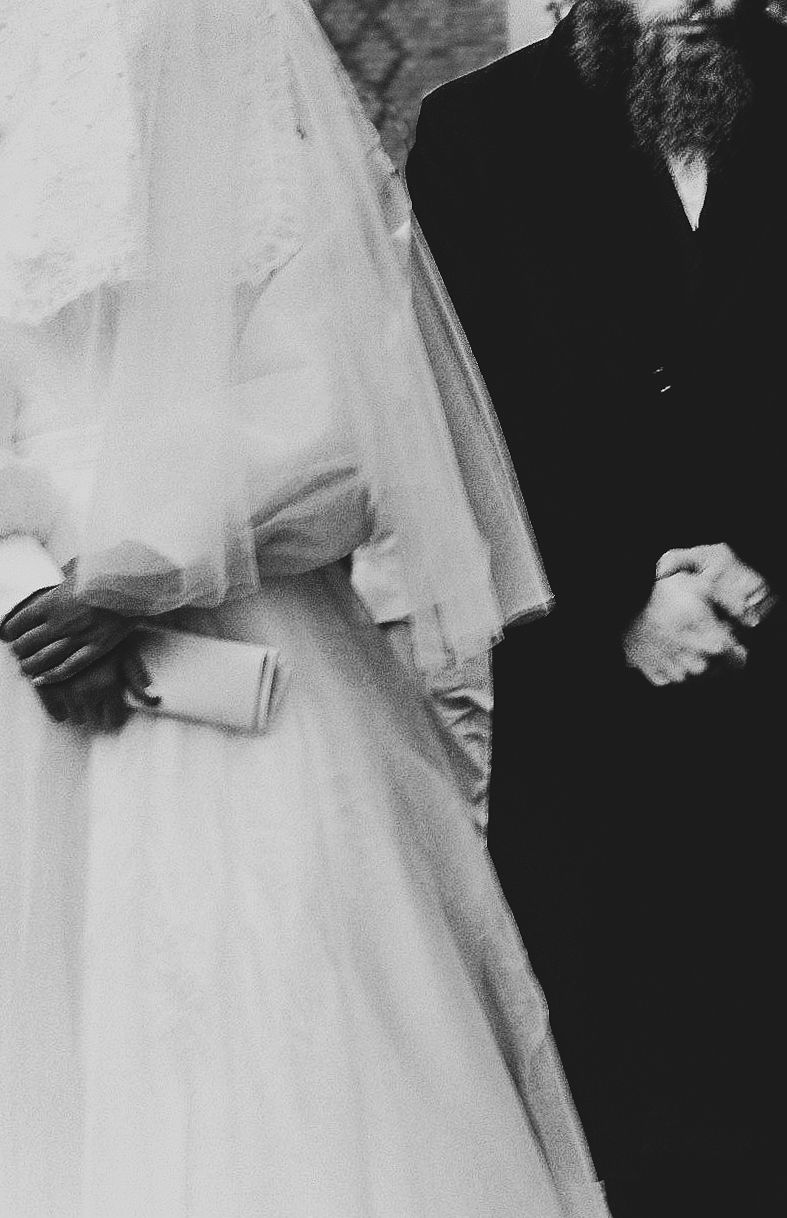A black and white wedding photograph showing the side profile of a bride in a flowing white veil and dress.