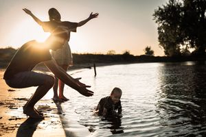 Silhouettes playing and splashing in a lake at sunset with golden light reflections.