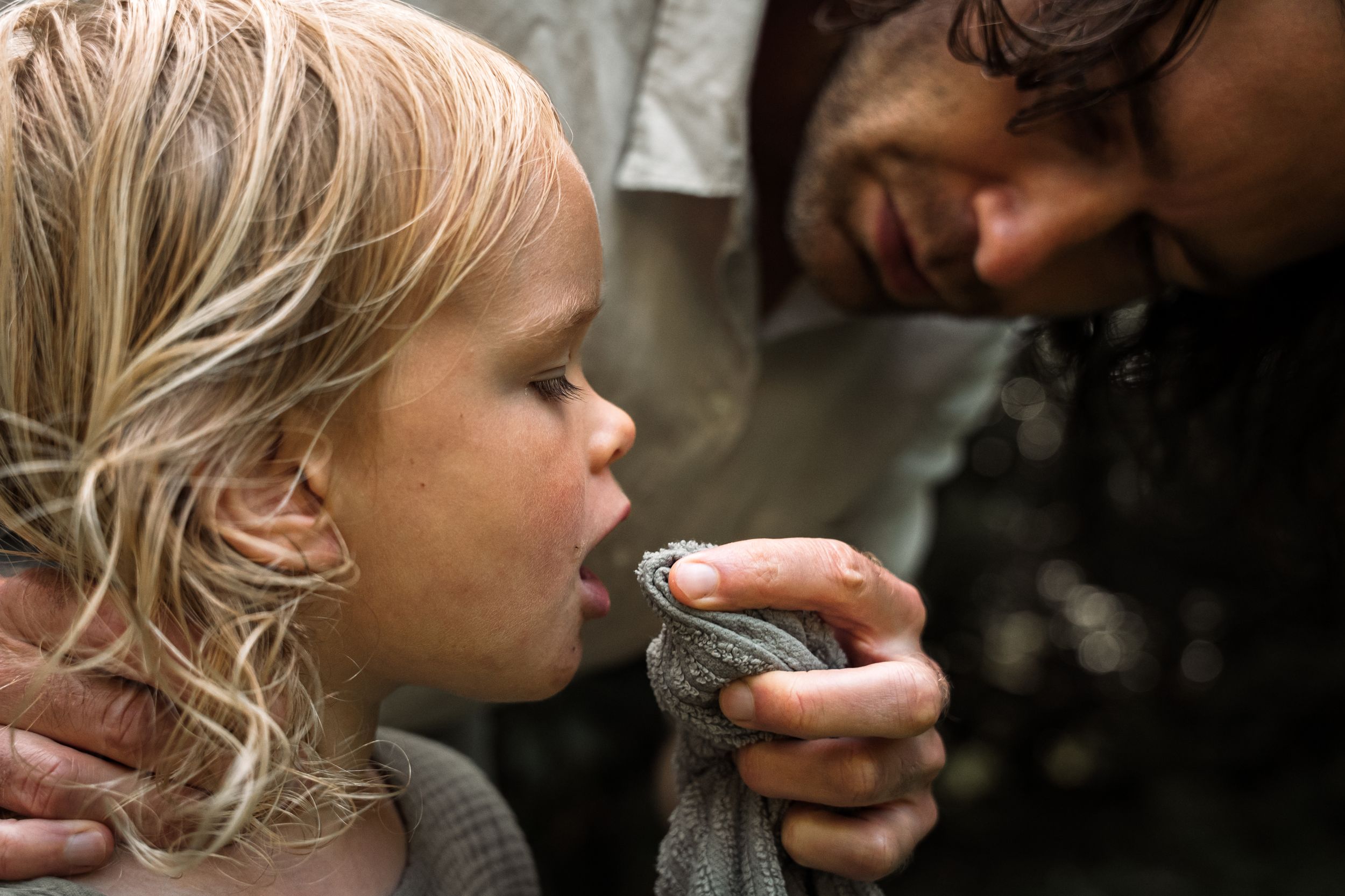A small child drinks from a metal cup in an intimate close-up shot.