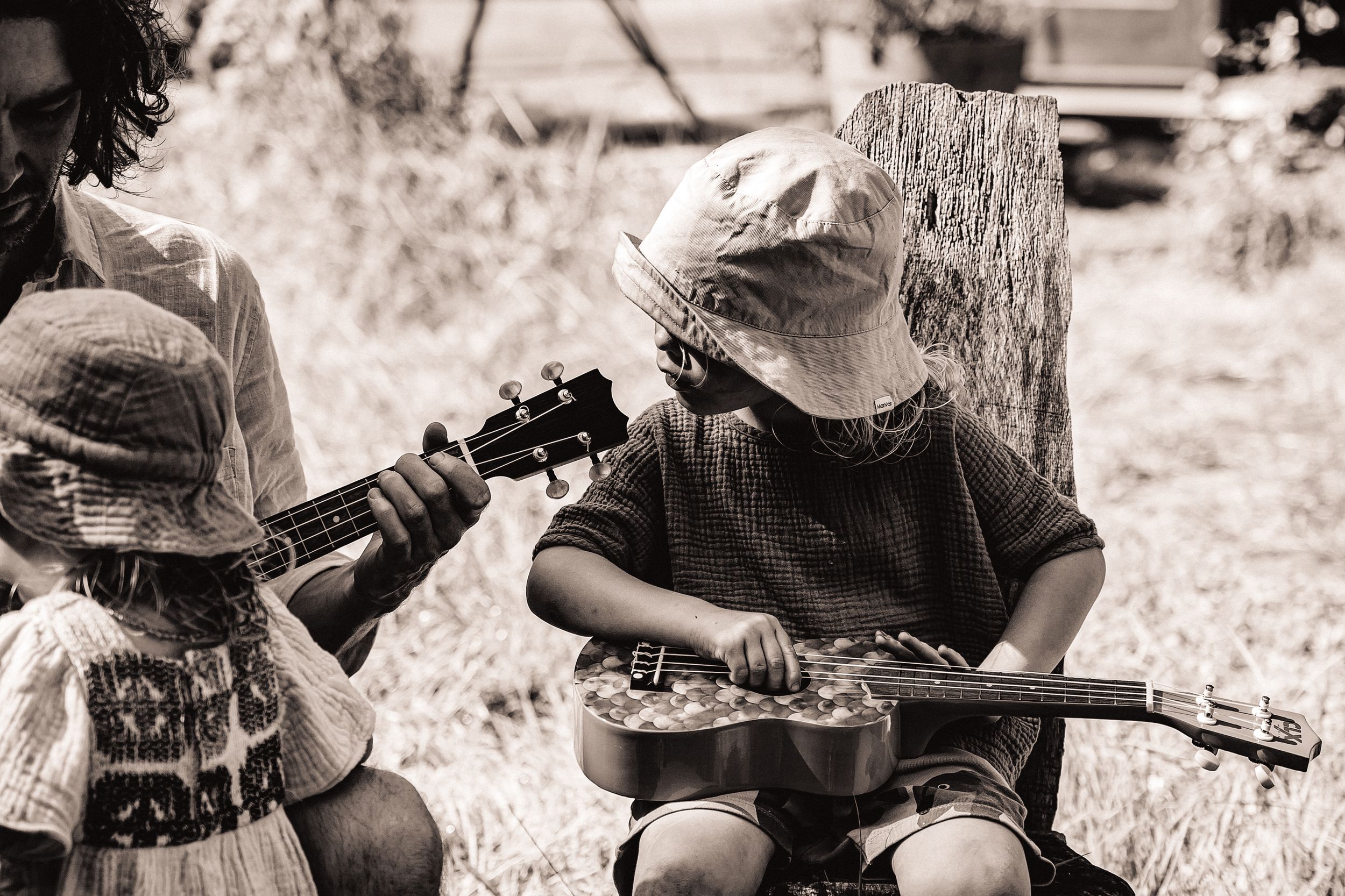 Children play musical instruments outdoors in black and white photography.
