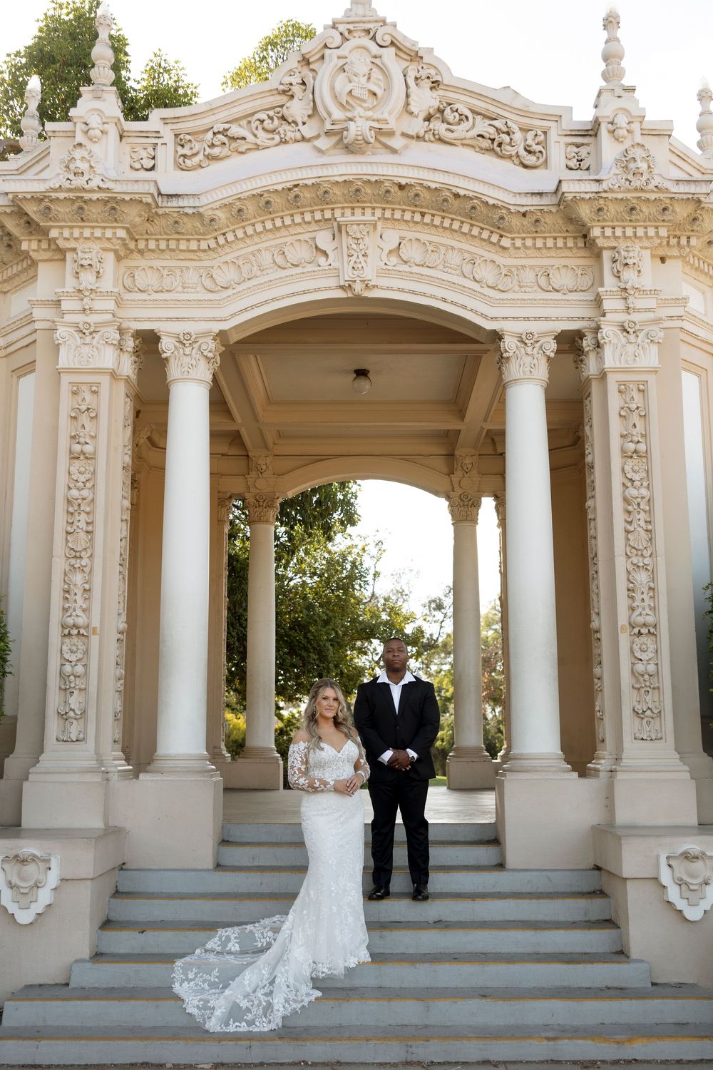 Wedding scene at an ornate white colonnade with decorative architectural details and stone steps.