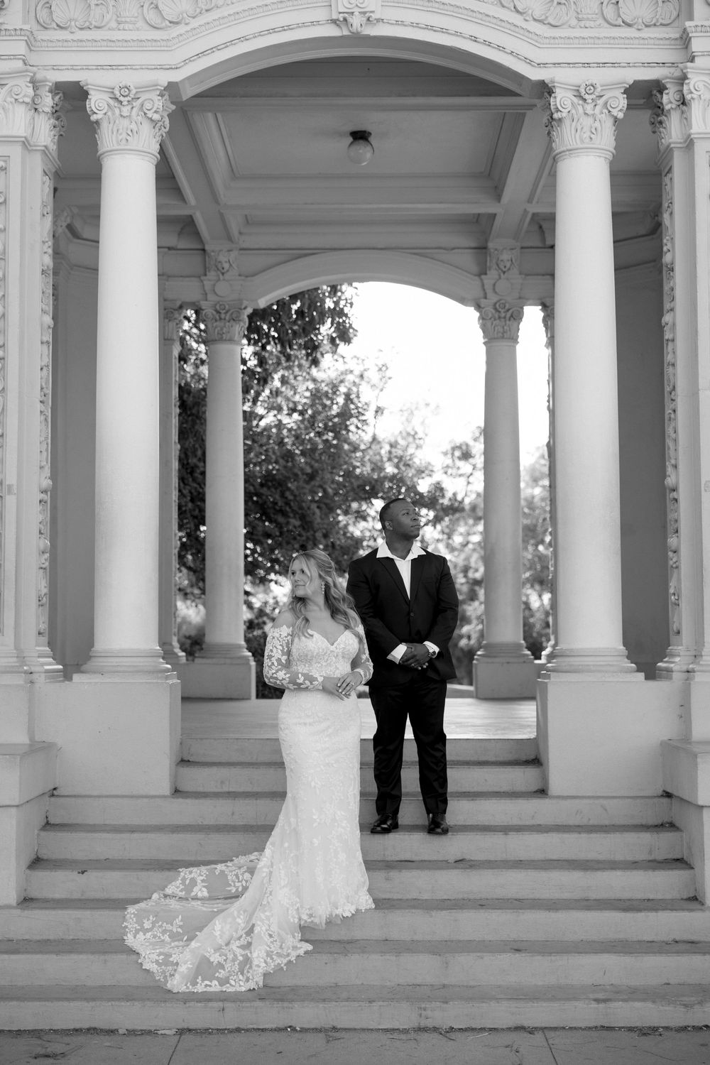 Wedding couple poses in an elegant white columned pavilion with ornate architectural details.
