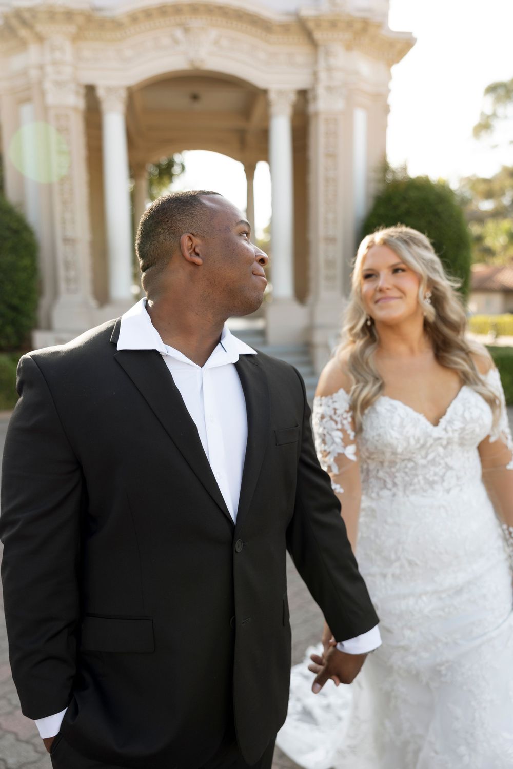 Romantic wedding couple sharing joyful moments under elegant white stone archways.
