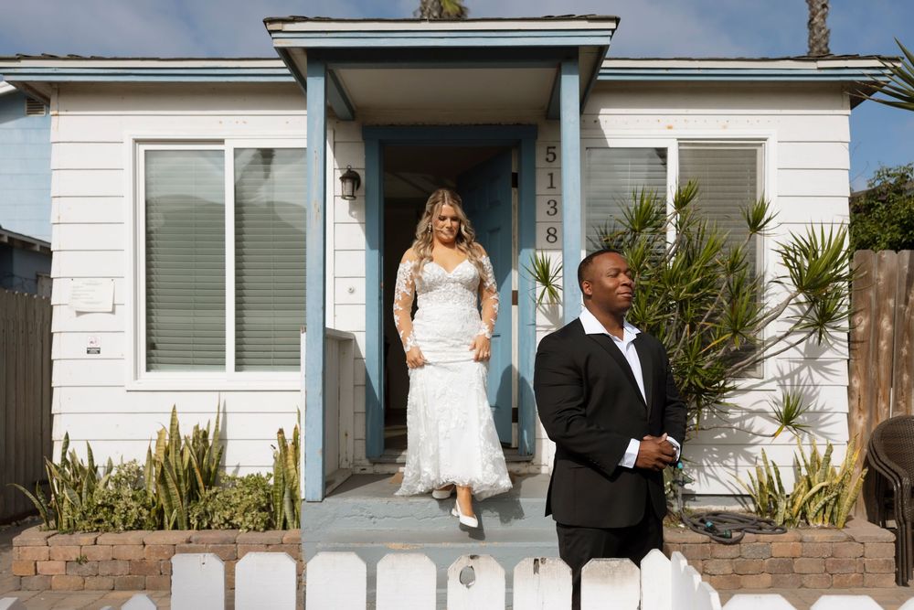 A couple stands together on a porch in formal wedding attire on their special day.
