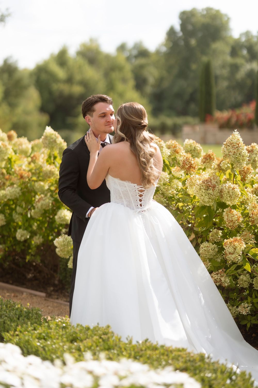 A couple shares a romantic moment among blooming vineyard rows on their wedding day.