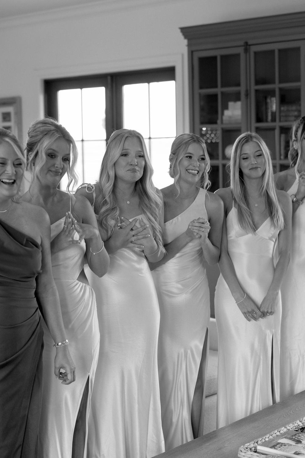 A group of bridesmaids in white dresses pose together indoors during a wedding celebration.