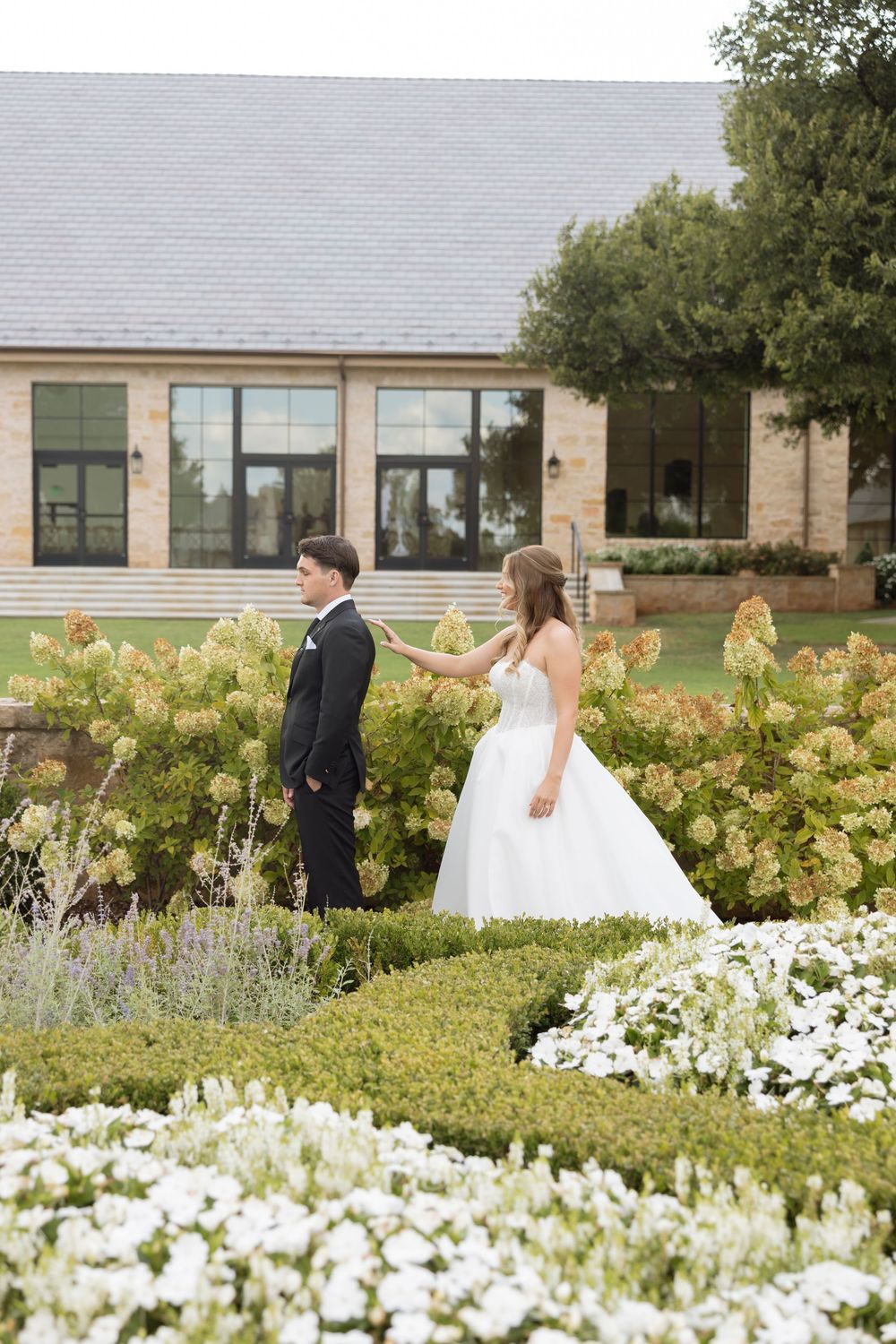 A wedding party walks through a garden filled with white flowers and lavender blooms on a sunny day.