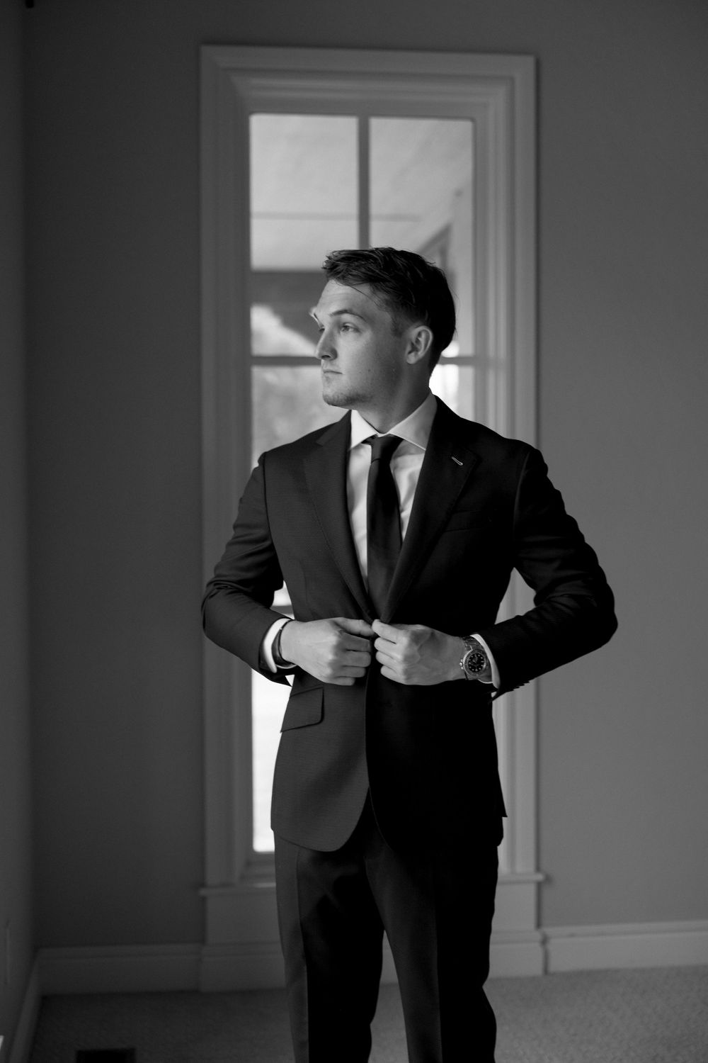 Black and white photo series of a groom adjusting his suit jacket and tie before the ceremony.