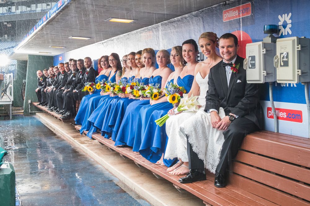 Sports team players and staff sitting together on blue benches in a dugout or sideline area in Citizens Bank Park