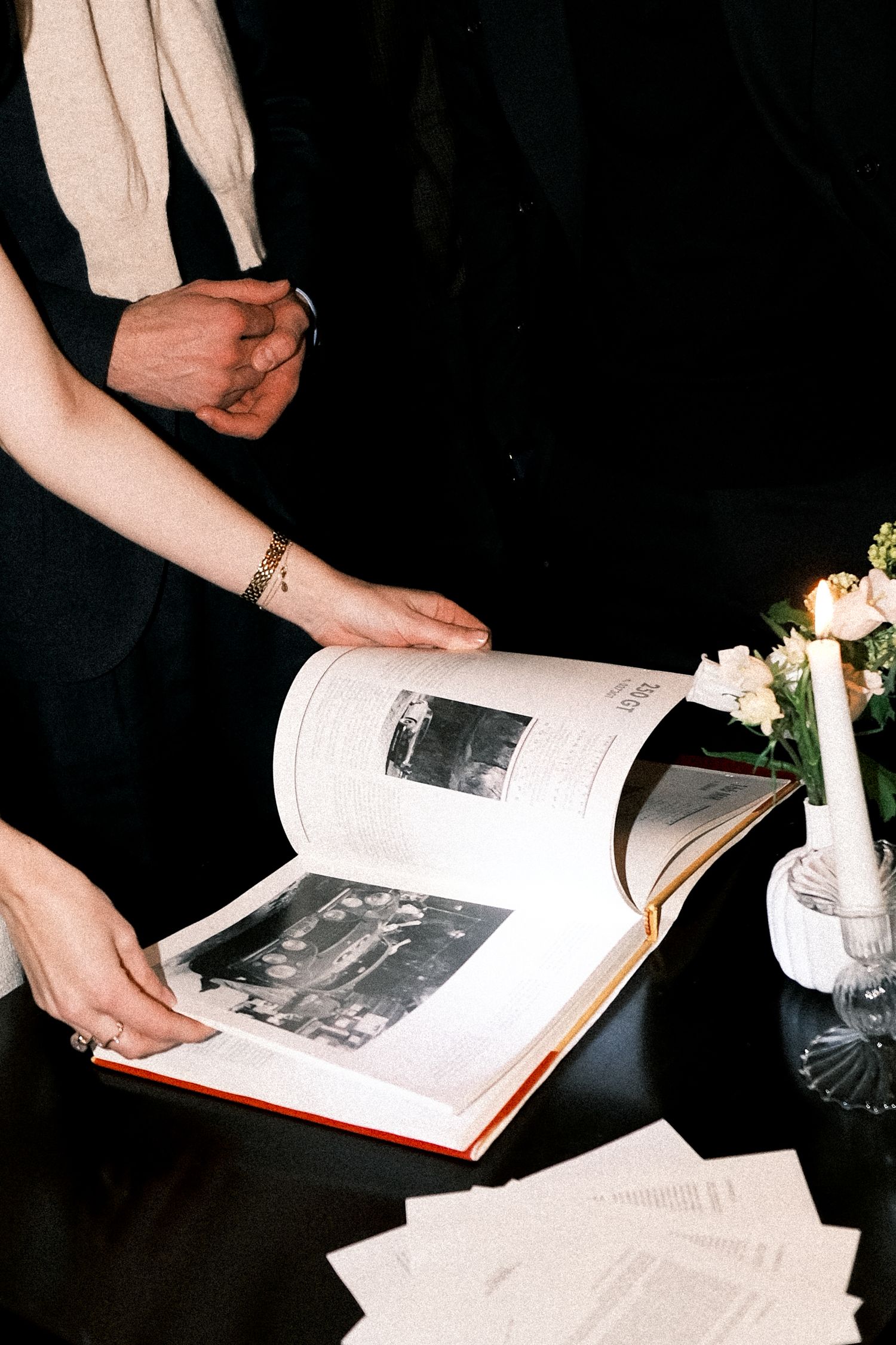 A series of hands flipping through pages of a book with flowers and candles visible in the dark background.