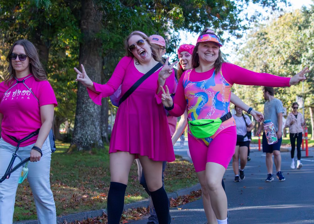 Group of participants in vibrant pink shirts showing enthusiasm during an outdoor charity walk event.