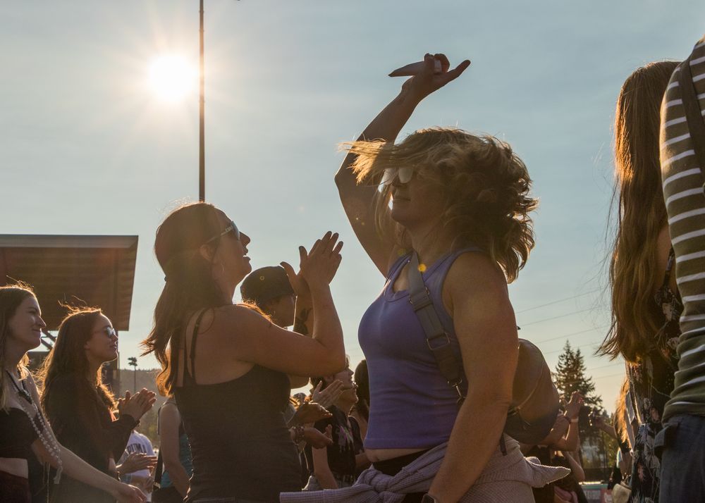 Silhouetted figures dance and celebrate outdoors at sunset during a festive summer gathering.