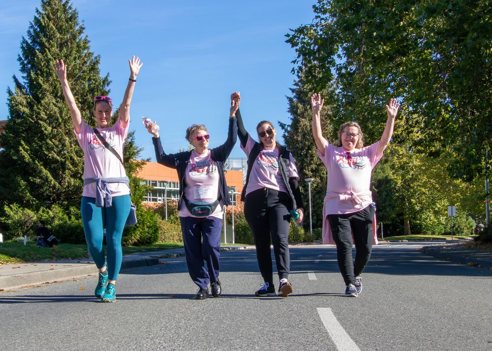 A group of participants wearing matching shirts celebrate joyfully during an outdoor charity walk event.
