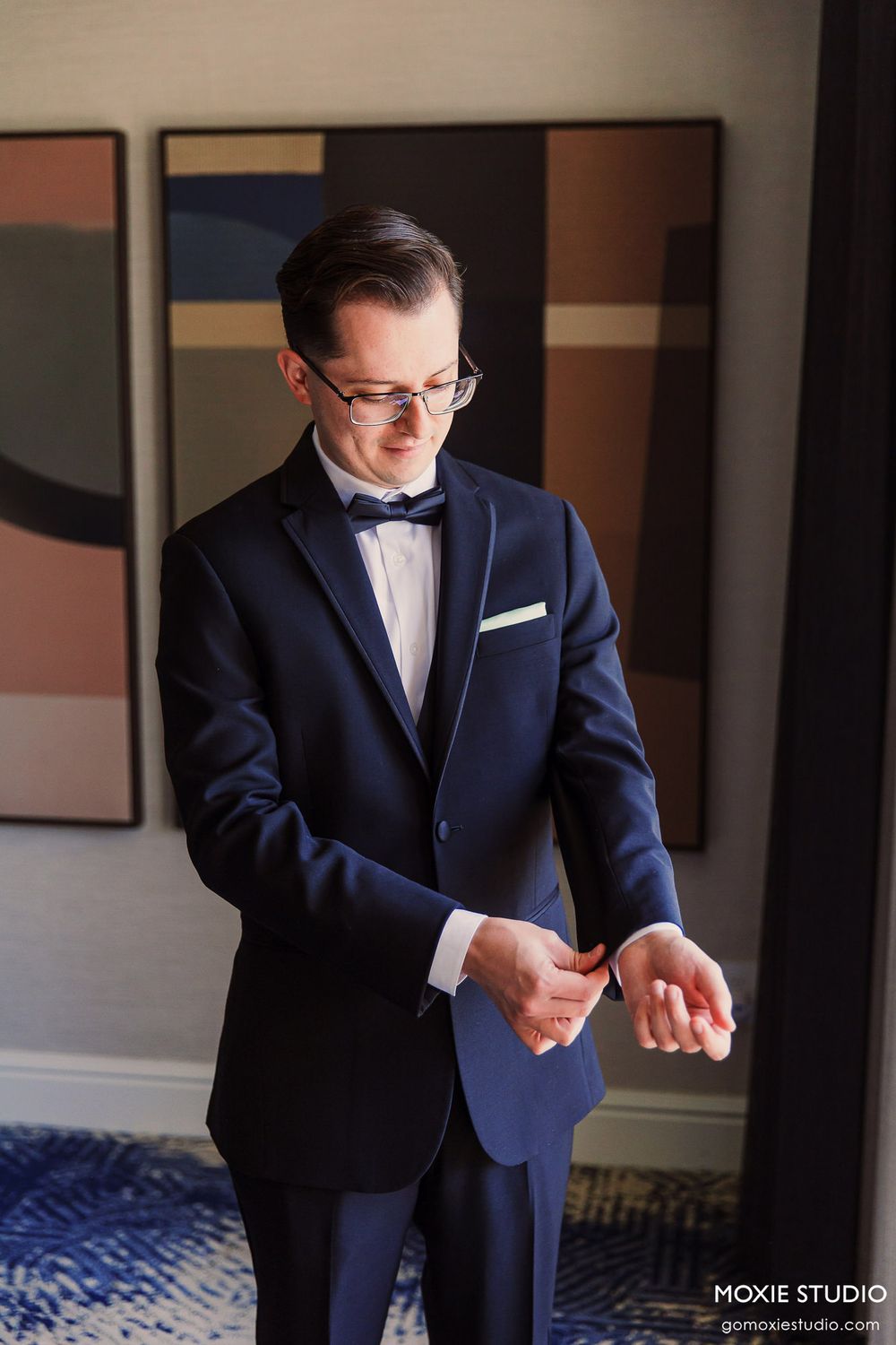 Multiple views of a groom adjusting his bowtie while wearing a classic navy tuxedo with white shirt.