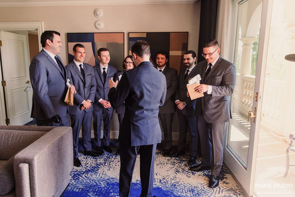 A group of men in blue suits stand in a hallway looking at something on the ground during a formal event.