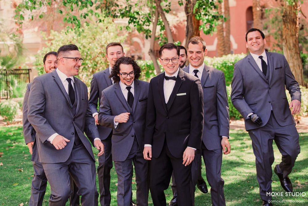 Groomsmen in navy suits share candid laughing moments in an outdoor garden setting.