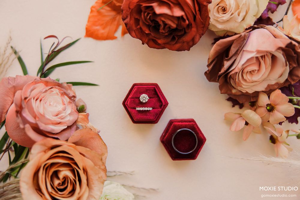 Elegant floral arrangement featuring peach and burgundy roses with delicate greenery against a light beige background.