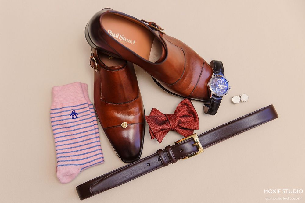 Wedding accessories including brown leather shoes, bow ties, and striped socks arranged on wooden surfaces.