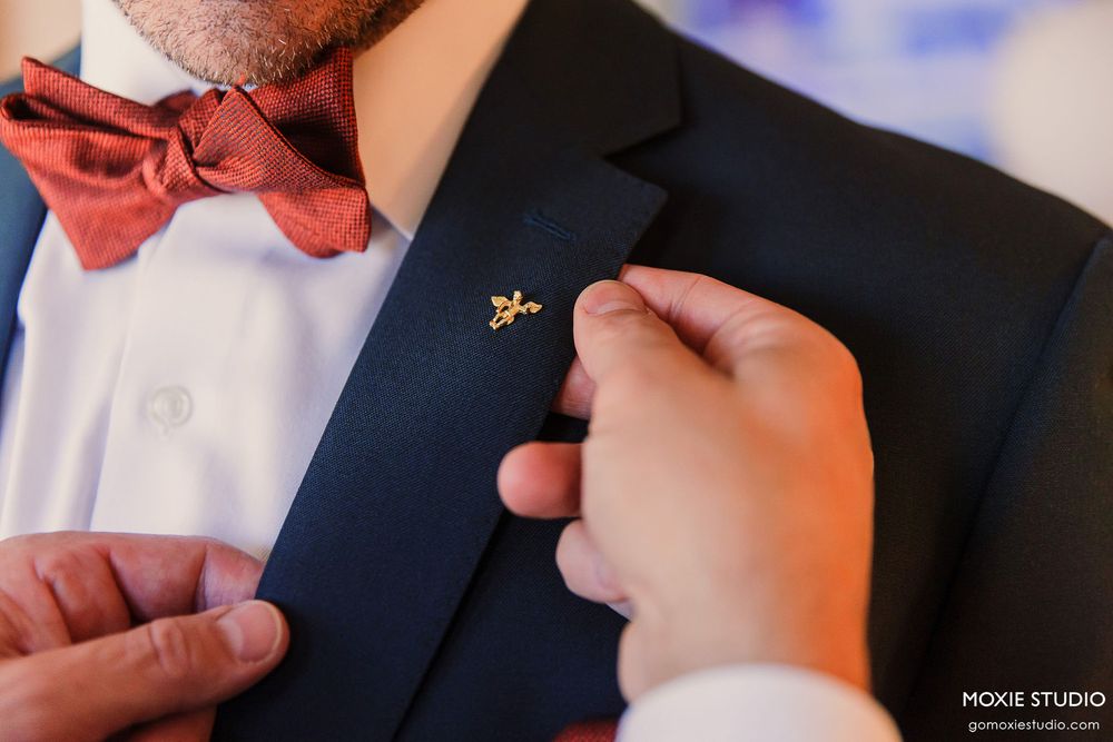 A groom adjusts his pink bow tie while getting ready in formal attire.
