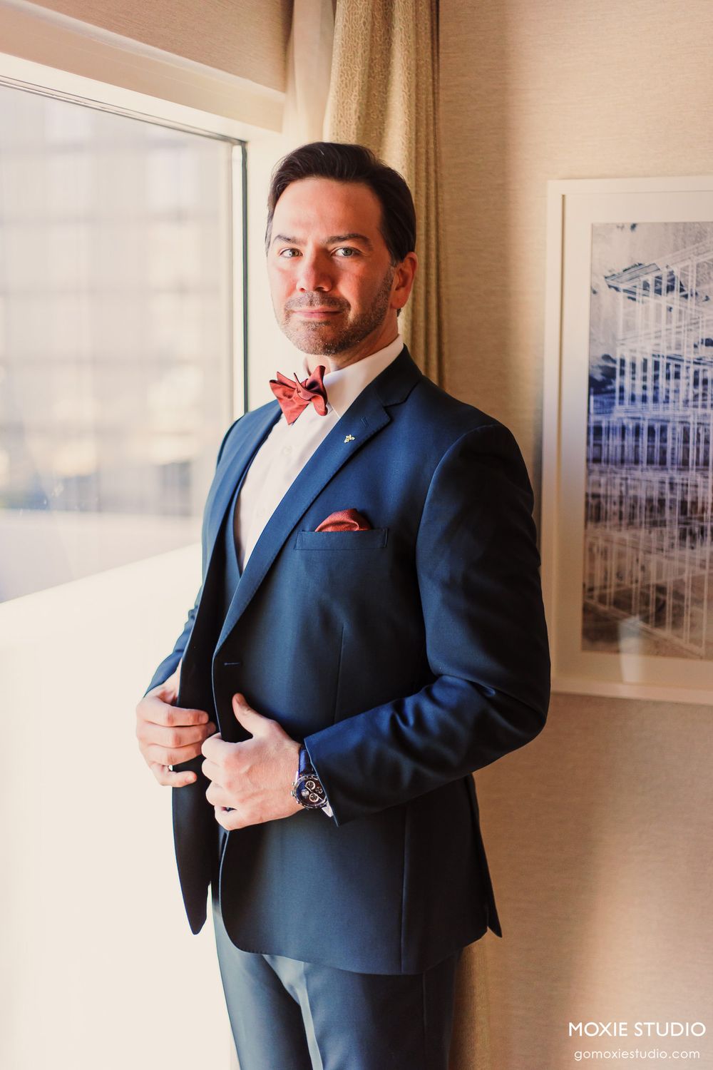 Elegant navy blue suit with red bow tie and pocket square in a room with framed artwork.