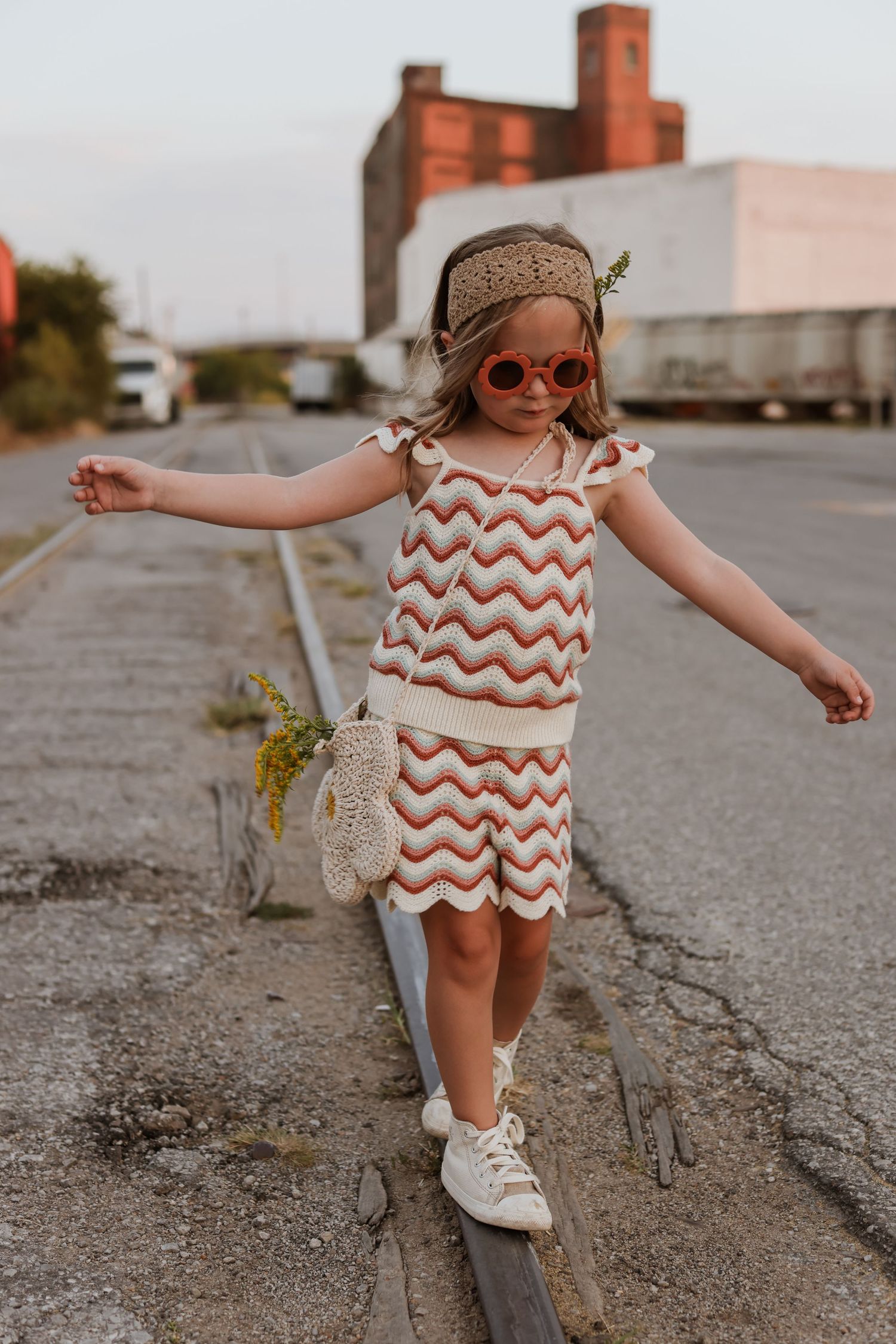 A little girl in striped crocheted set balances on abandoned train tracks at an urban family photo session in Kansas City.