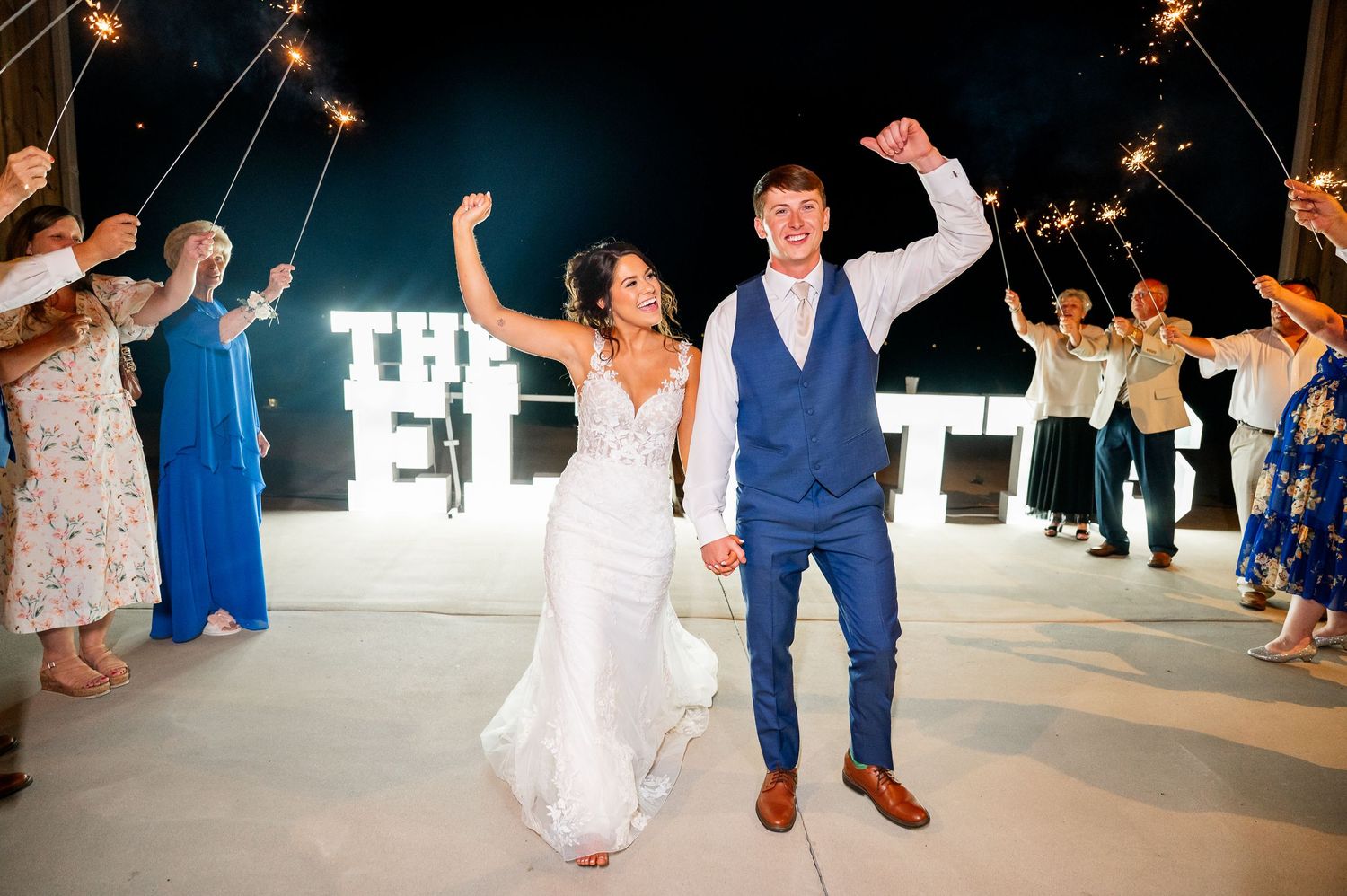Wedding celebration with guests dancing under illuminated outdoor lighting.