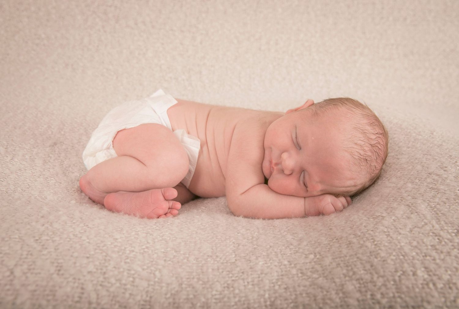 Newborn curled up on her front.