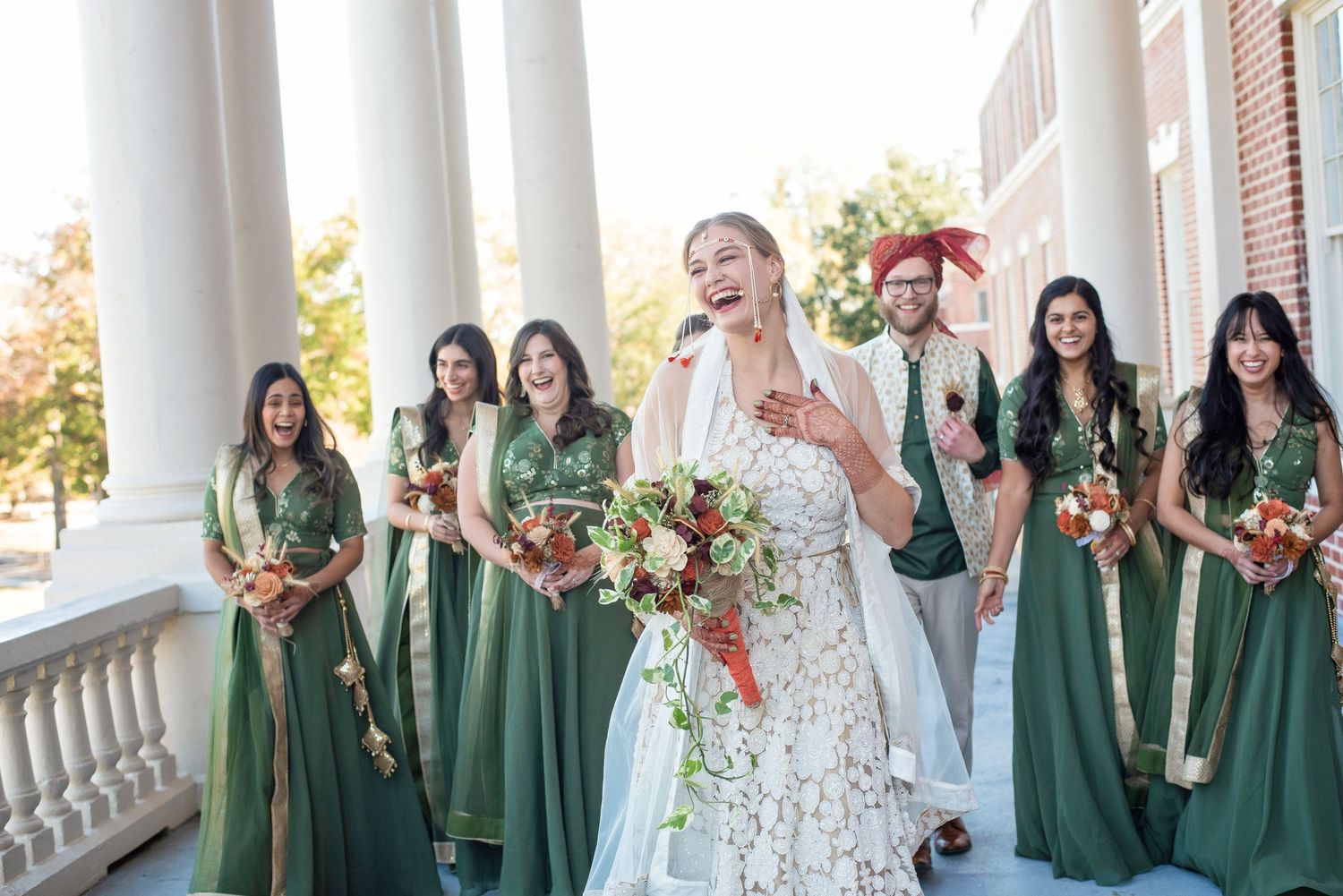 Bridal party in elegant green dresses posing on columned porch.
