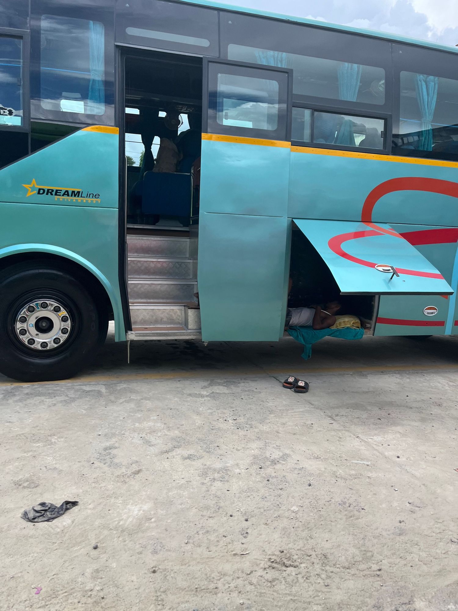 A turquoise and orange tourist bus with open door parked on a dirt surface.