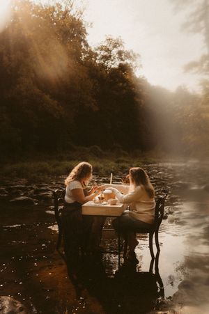 Two people share a romantic dinner at a table set in a misty river during golden hour sunset.