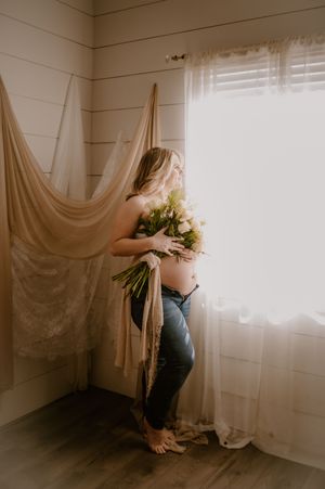 A dreamy boudoir scene with soft window light filtering through sheer curtains in a minimalist white room.