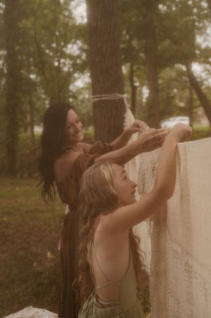 A person in a sleeveless top dances expressively in a wooded outdoor setting during golden hour.