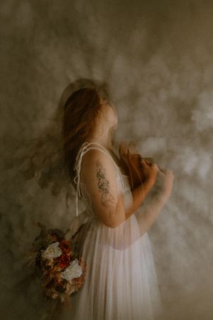 Ethereal bridal portraits with bouquet and white dress against moody backdrop.