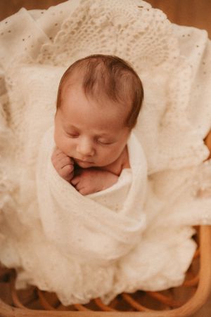 A sleeping newborn baby wrapped in soft white blankets with a sepia-toned background.