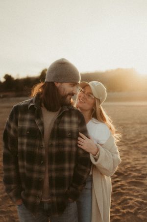 A romantic couple embraces during golden hour in a field, with warm sunlight creating a dreamy atmosphere.