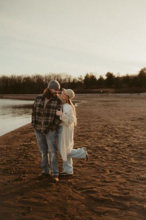 A couple in casual attire walks along a sandy beach at sunset, creating a romantic silhouette against the dusky sky.