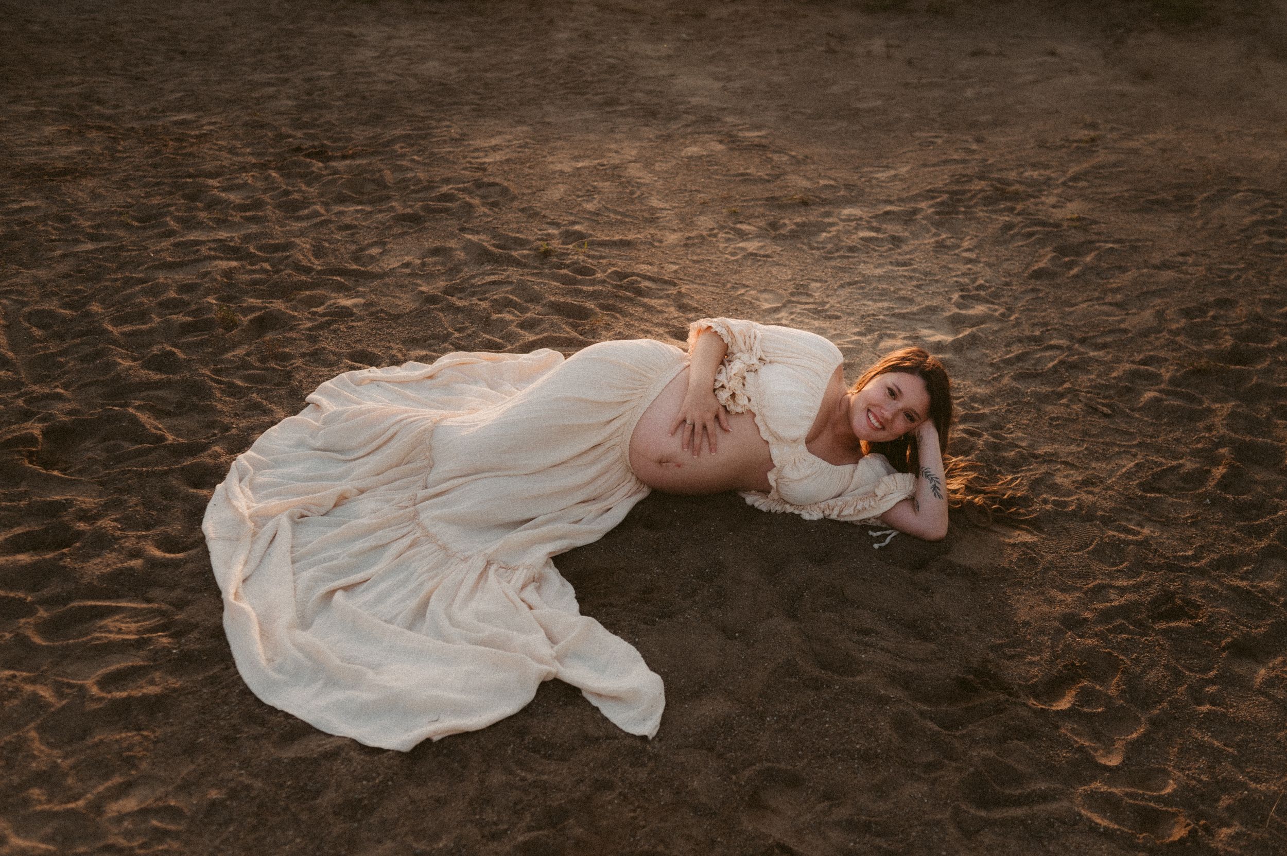 A person in a flowing white dress lies gracefully on dark earth surrounded by fallen autumn leaves.