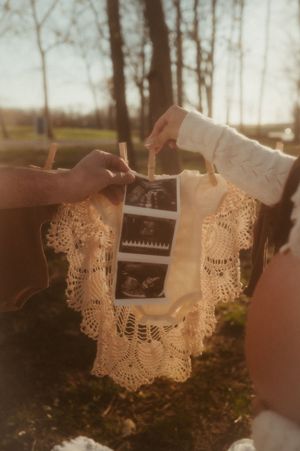 Hands hanging delicate white lace fabric on a clothesline outdoors during golden hour sunlight.