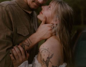 A romantic couple with tattoos share an intimate moment outdoors in soft lighting.