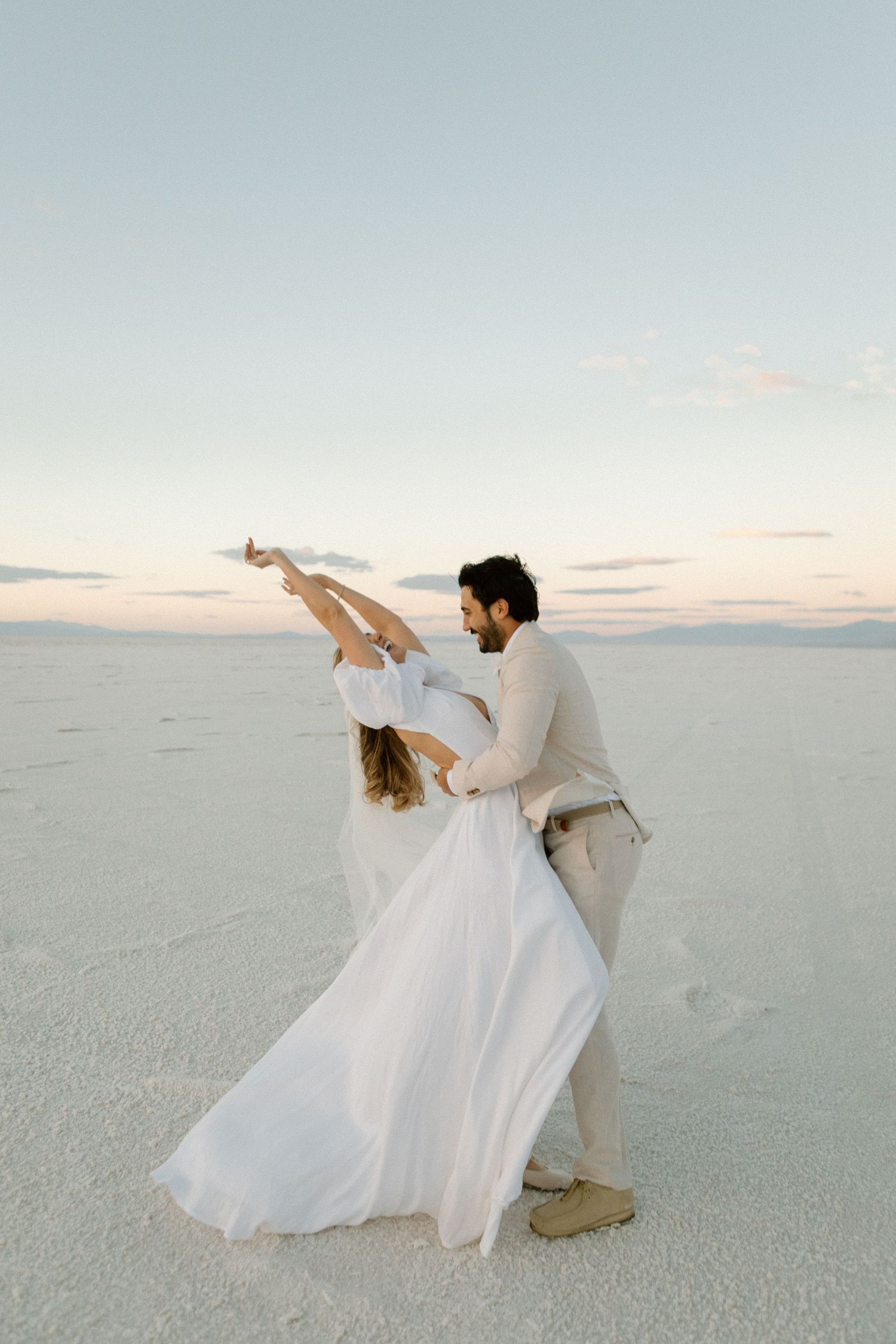 Couple dances gracefully on salt flats during sunset wedding photoshoot.