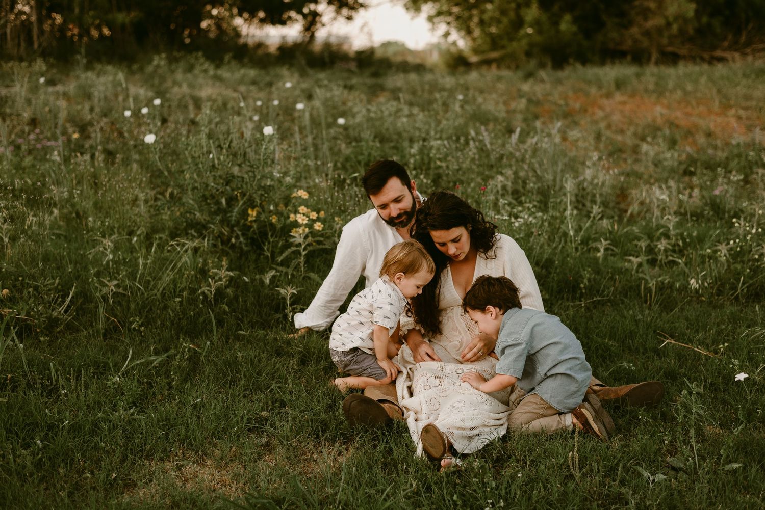 A family sits together on a blanket in a wildflower meadow at sunset enjoying an intimate outdoor moment.