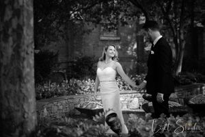 A romantic black and white photo of a couple in formal attire standing in a garden setting.