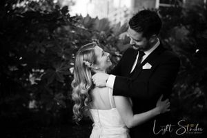 A romantic black and white photograph of newlyweds embracing during their wedding celebration in a garden setting.