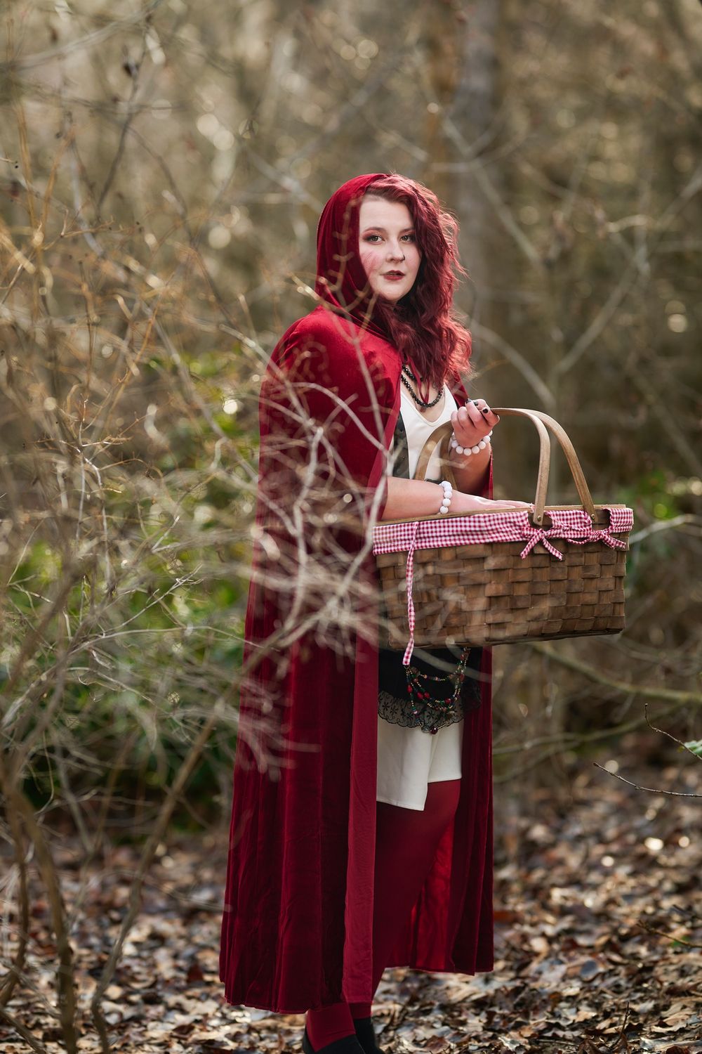 A person in a red velvet cloak carries a picnic basket through a misty autumn forest setting.