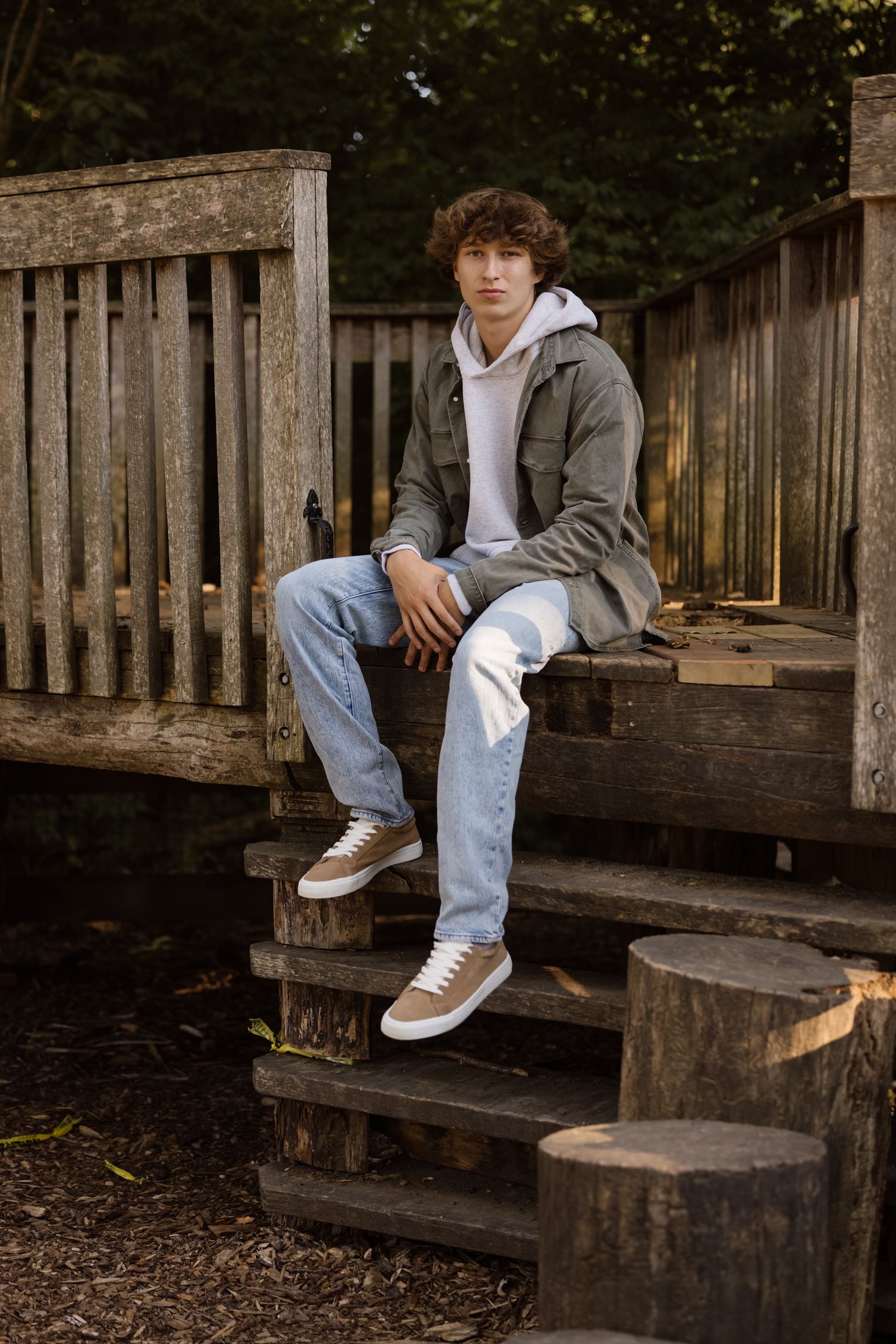 A casual portrait on wooden steps showing someone in a gray jacket and jeans.