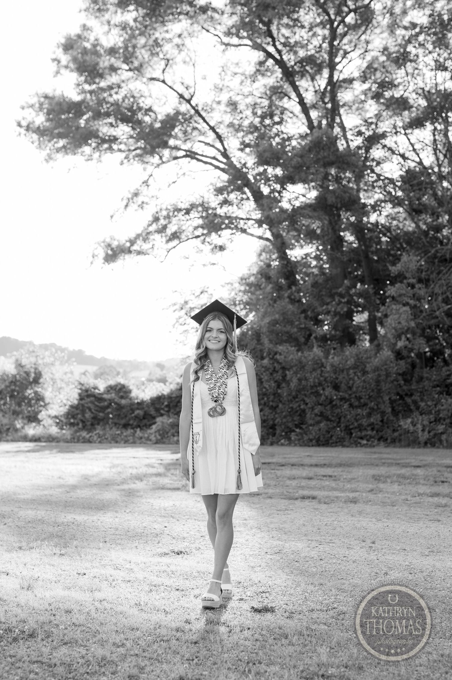 Black and white graduation portrait showing graduate in casual dress and cap outdoors.