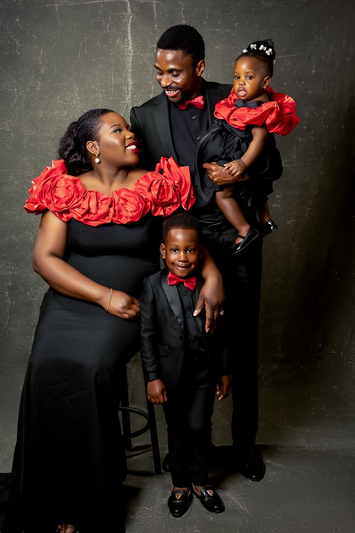 Studio portrait of family in formal black attire with red ruffle accents against dark background.